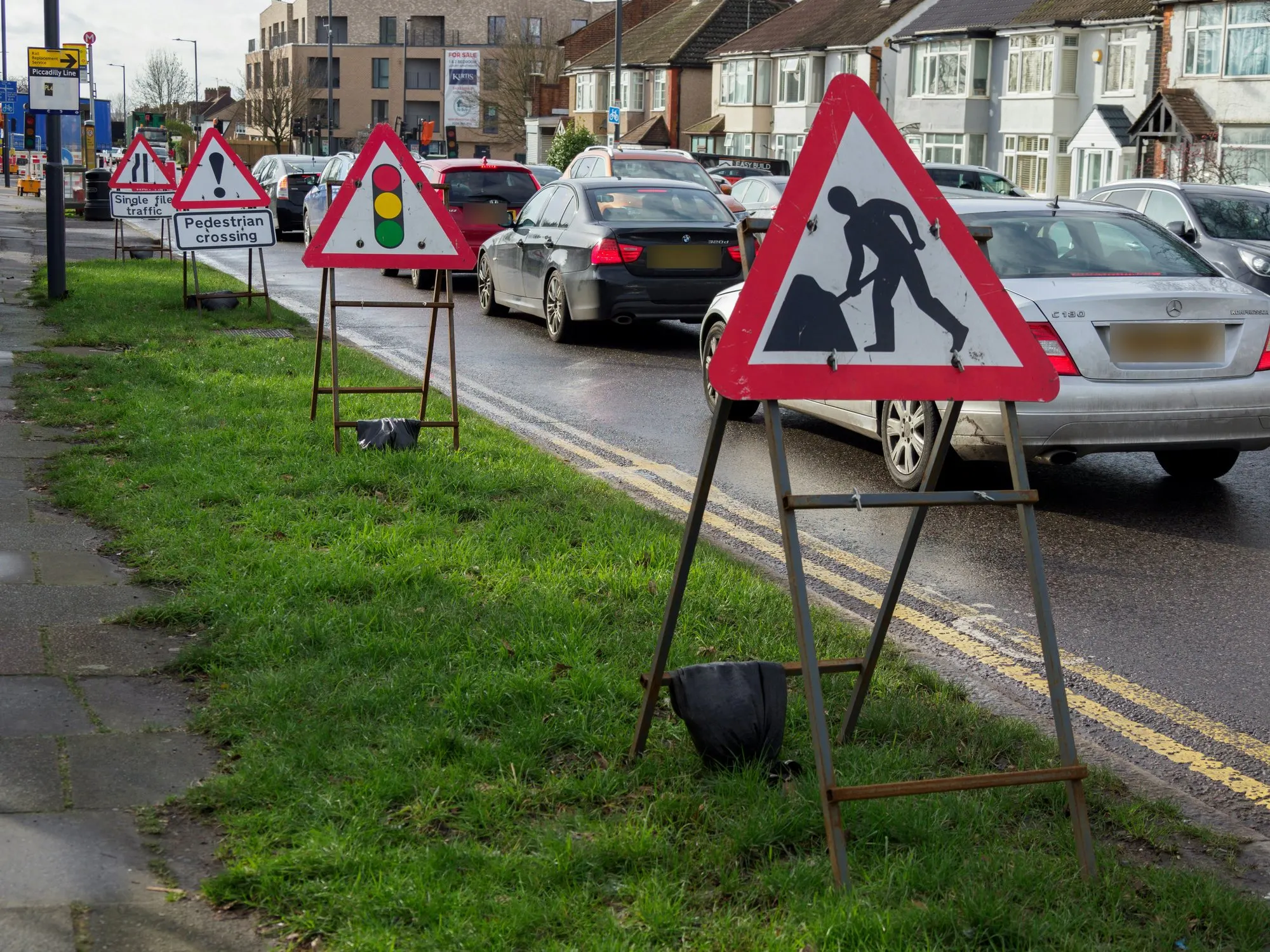Roadworks warning signs set out on a grass verge beside queuing traffic